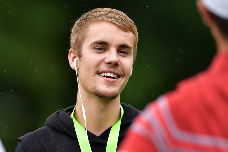Justin Bieber, wearing earbuds, smiling.